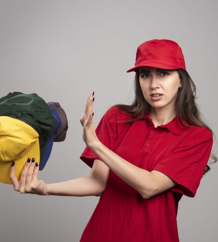 Delivery woman in red uniform staying away from colorful caps. High quality photo